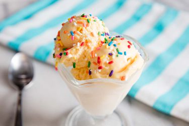 Closeup of a glass goblet containing several scoops of no-churn vanilla ice cream, topped with rainbow sprinkles.