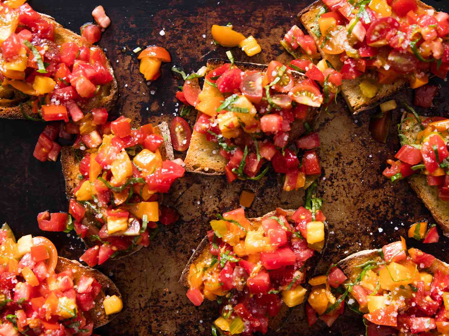 Overhead view of the finished bruschetta assembled on a well-used rimmed baking sheet.