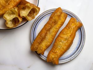 Youtiao on a plate next to a platter of youtiao