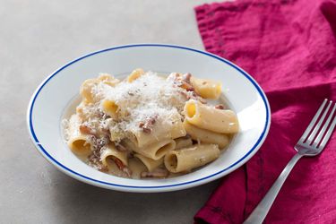 A white bowl of Pasta alla Gricia topped with shredded cheese