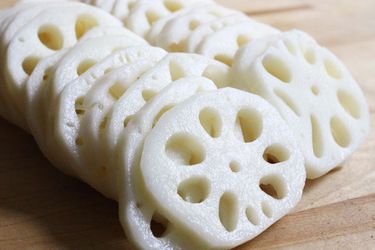 Slices of lotus root shingled on a wooden cutting board.