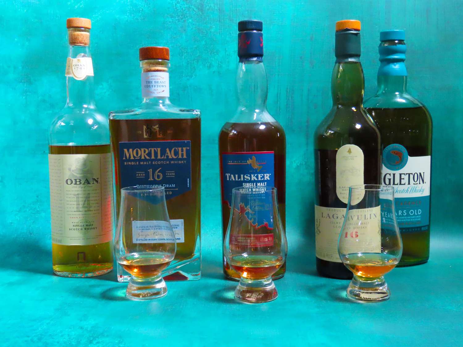 multiple bottles of whisky and whisky tasting glasses on a blue surface