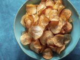 A blue ceramic bowl of potato chips on a blue background.