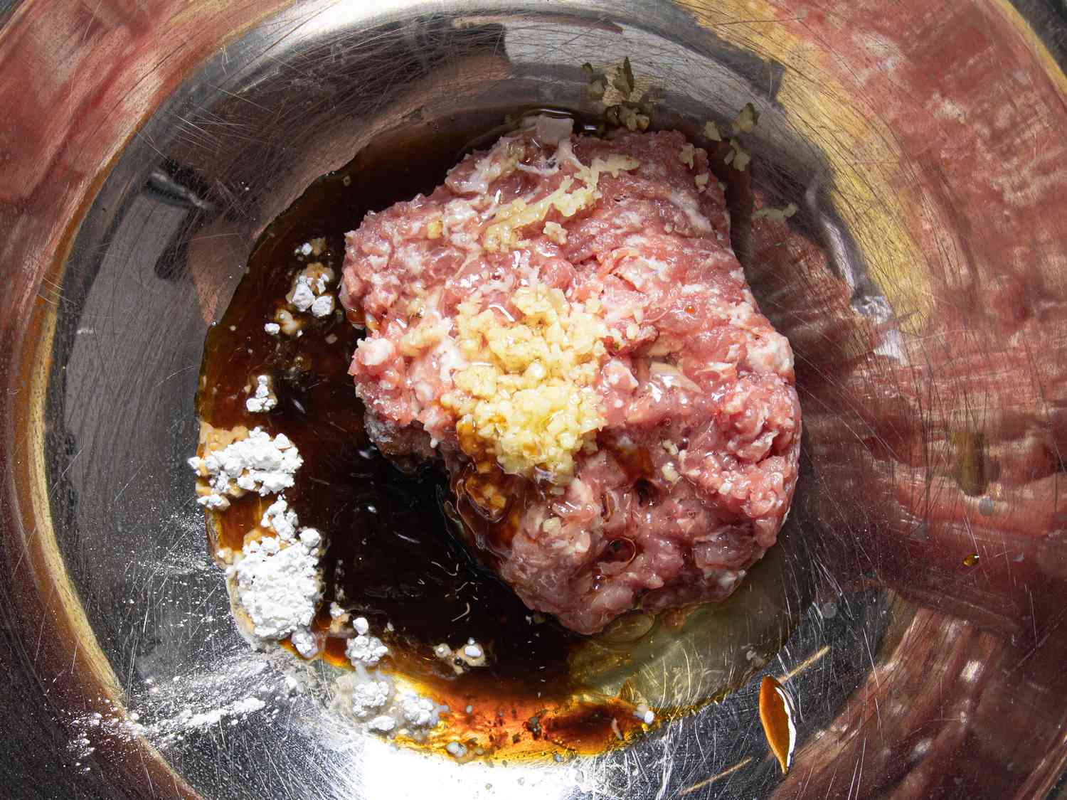 Ground pork with ginger, cornstarch, and other aromatics in a stainless steel bowl.