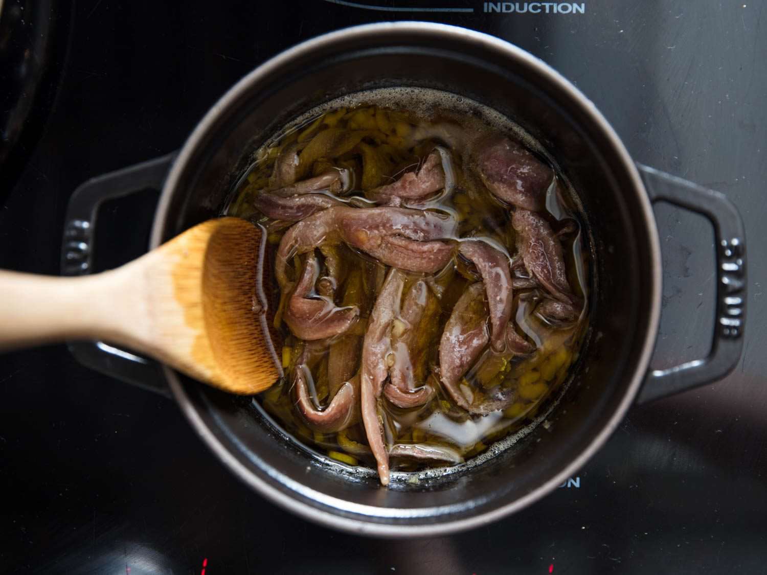 木勺搅拌着一锅漂浮在橄榄油中的凤尾鱼。gydF4y2Ba