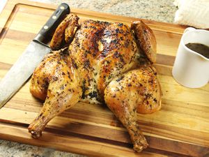 在切菜板上涂上香草的烤鸡，配上一把刀和一锅肉汁。