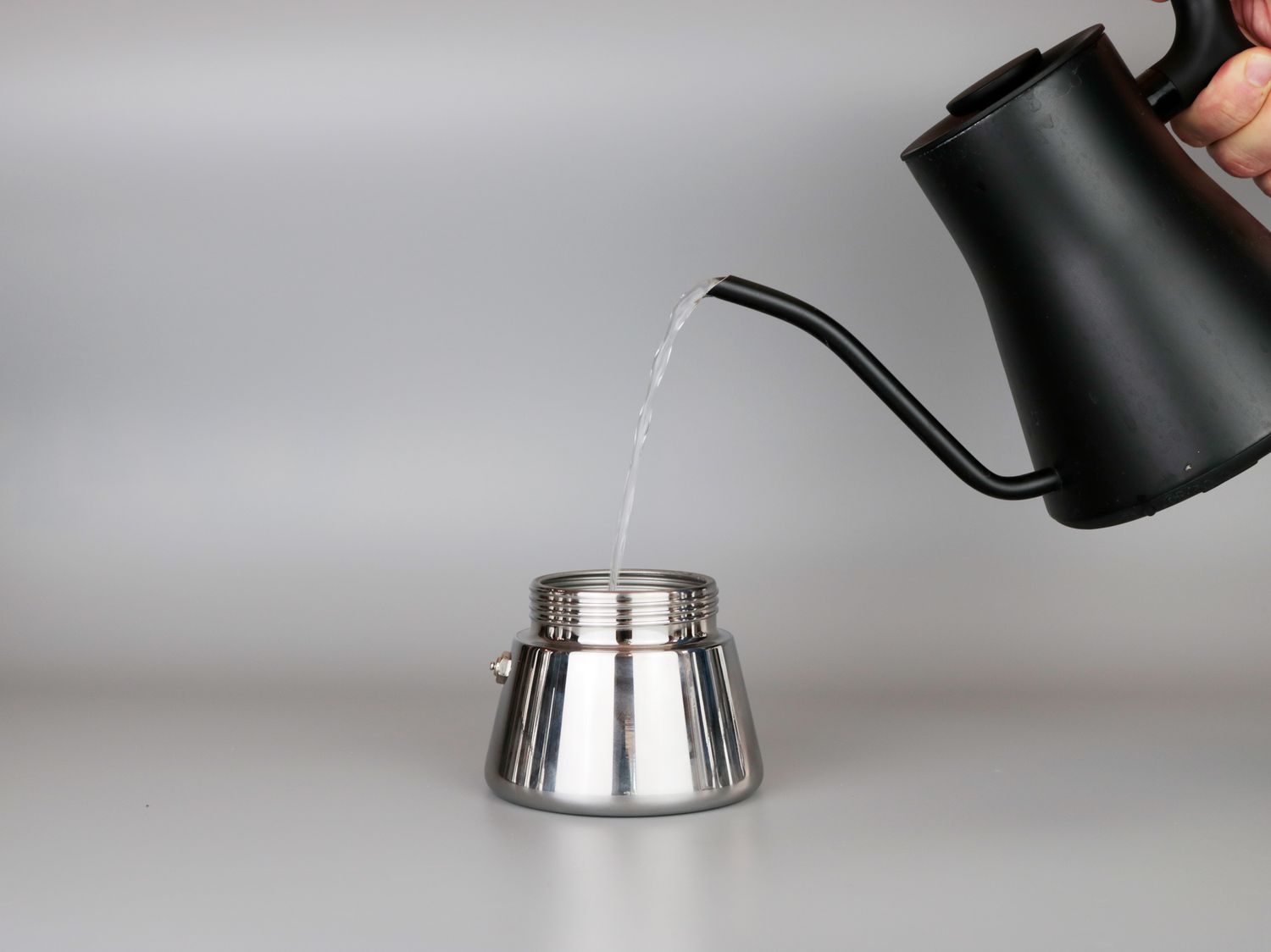 a kettle pouring water into the base of a moka pot