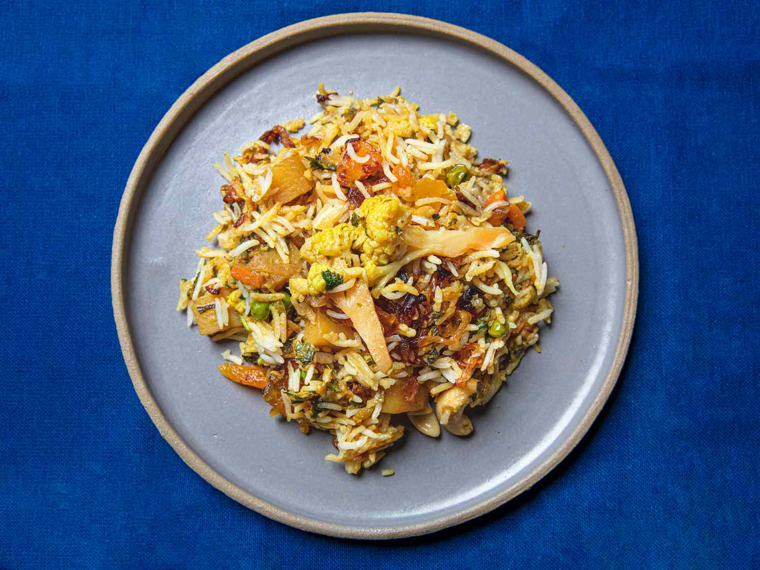 A plated portain of Biryani on a pale purple plate on a bright blue background