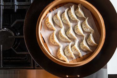 Overhead view of a bamboo steamer filled with dumplings set in a wok, ready to be steamed.