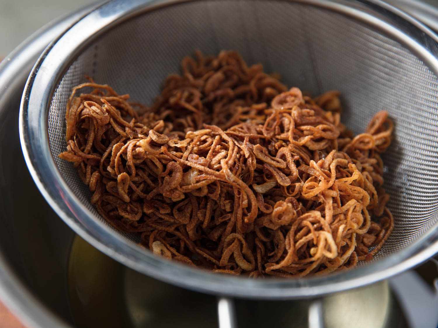 Crispy fried shallots in a metal strainer