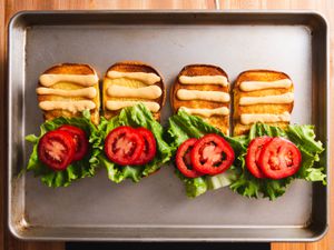 四个烤好的汉堡包放在烤盘上，每个包的上半部分都有三道自制的沙司，下半部分是生菜和番茄。