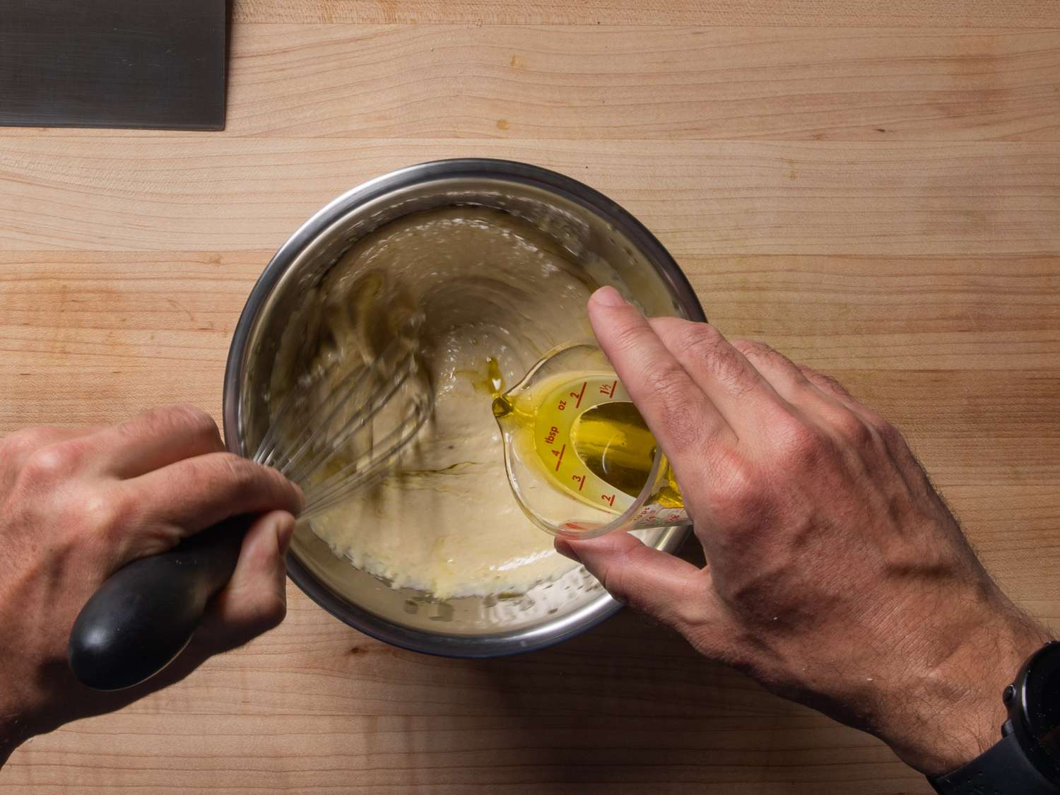 Whisking while drizzling the olive oil into the dressing in a mixing bowl.