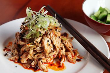 A mound of Sichuan chicken salad garnished with scallions and black sesame on a plate with chopsticks.