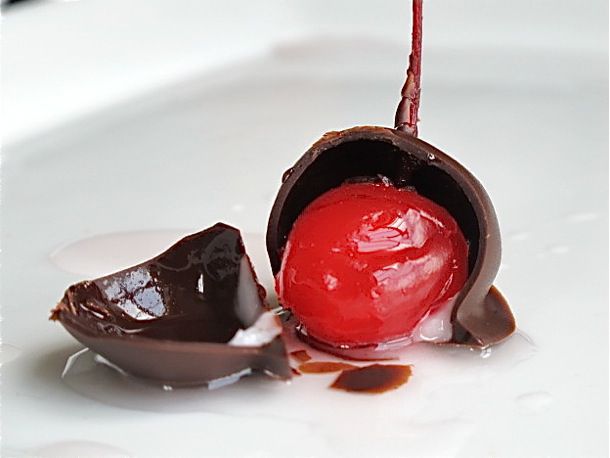 A broken chocolate cherry cordial with a bright red cherry.