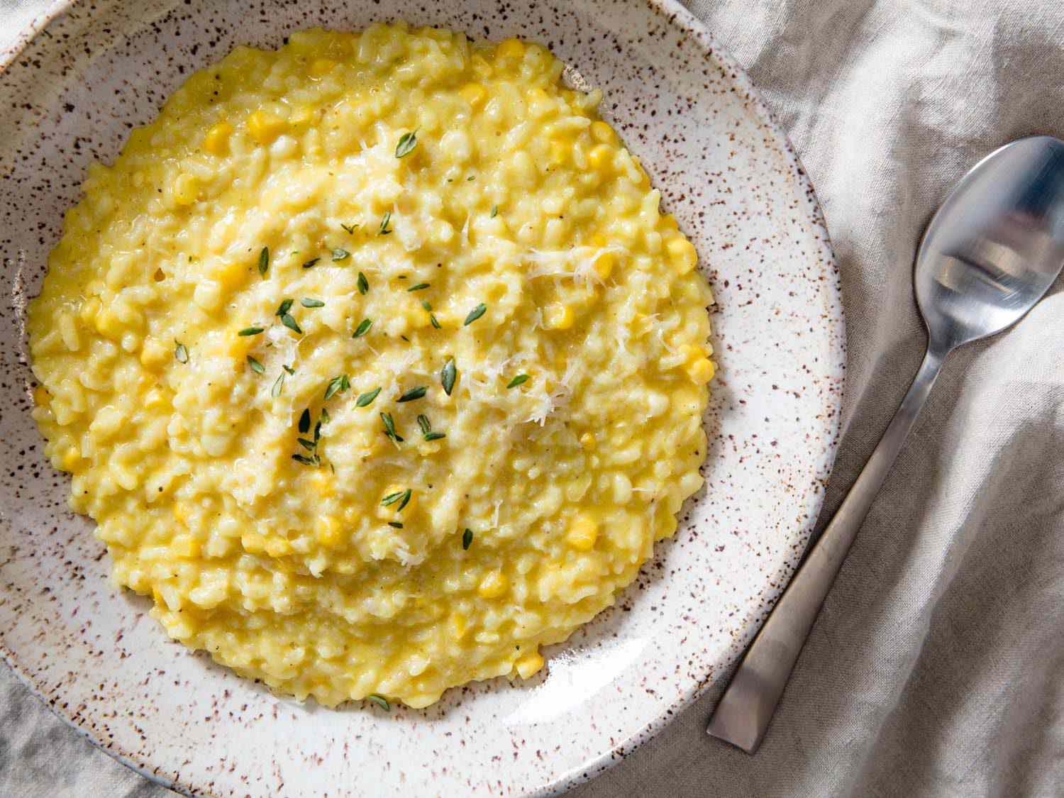 Overhead view of pressure cooker corn risotto in a shallow bowl next to a spoon.