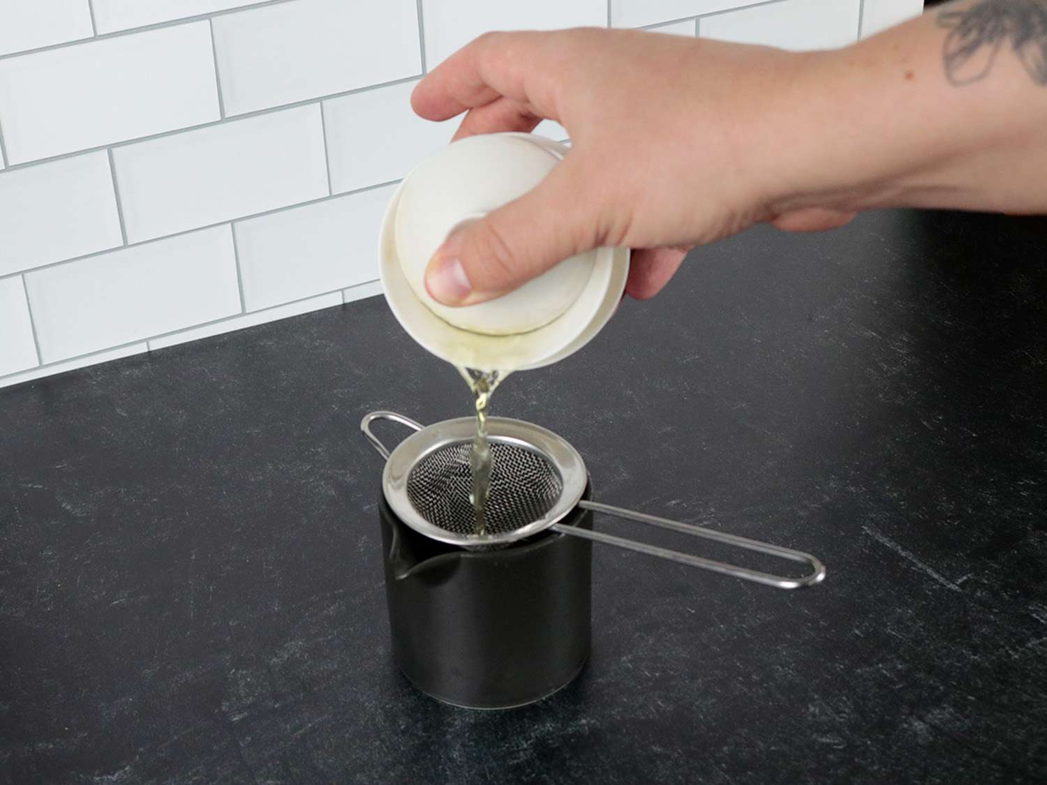 a gaiwan tea brewer pours tea through a small fine mesh strainer into a carafe