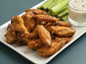 Oven-fried buffalo wings on a white rectangular plate with celery sticks and a glass cup of bleu cheese dressing.