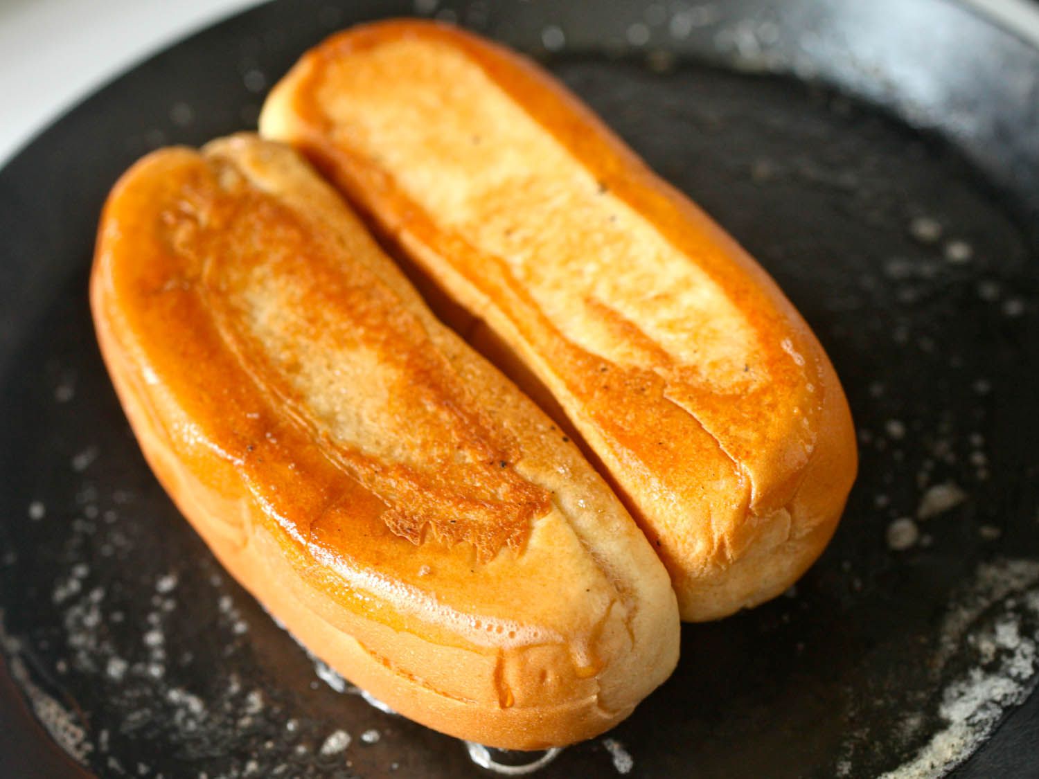 在涂满黄油的煎锅里烤分顶热狗面包。