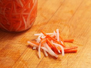 一罐越南腌白萝卜和胡萝卜，用来装饰越南越菜。坛子前的木柜台上放着一小堆腌蔬菜。