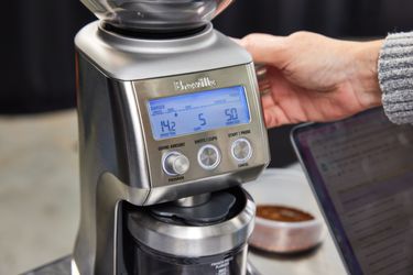 一个person adjusting the grind setting of a breville coffee grinder