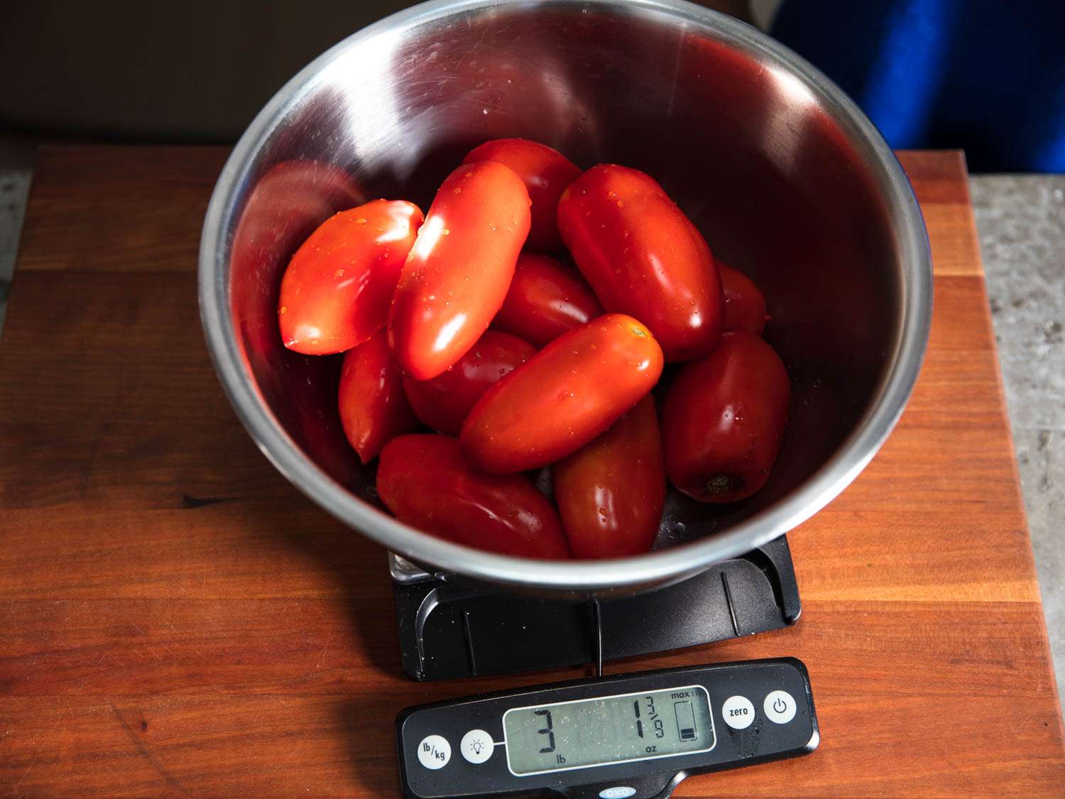 Washed plum tomatoes being weighed in a metal bowl on a digital scale