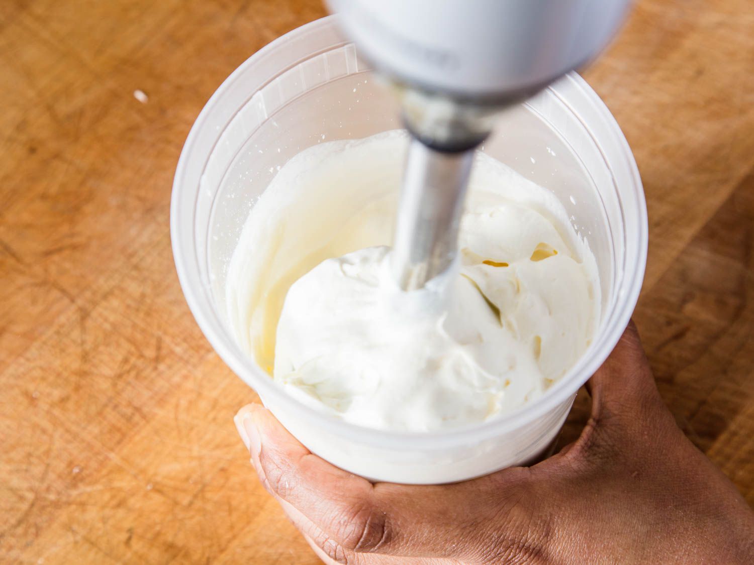 用浸入式搅拌器在一个透明的塑料容器中搅拌奶油