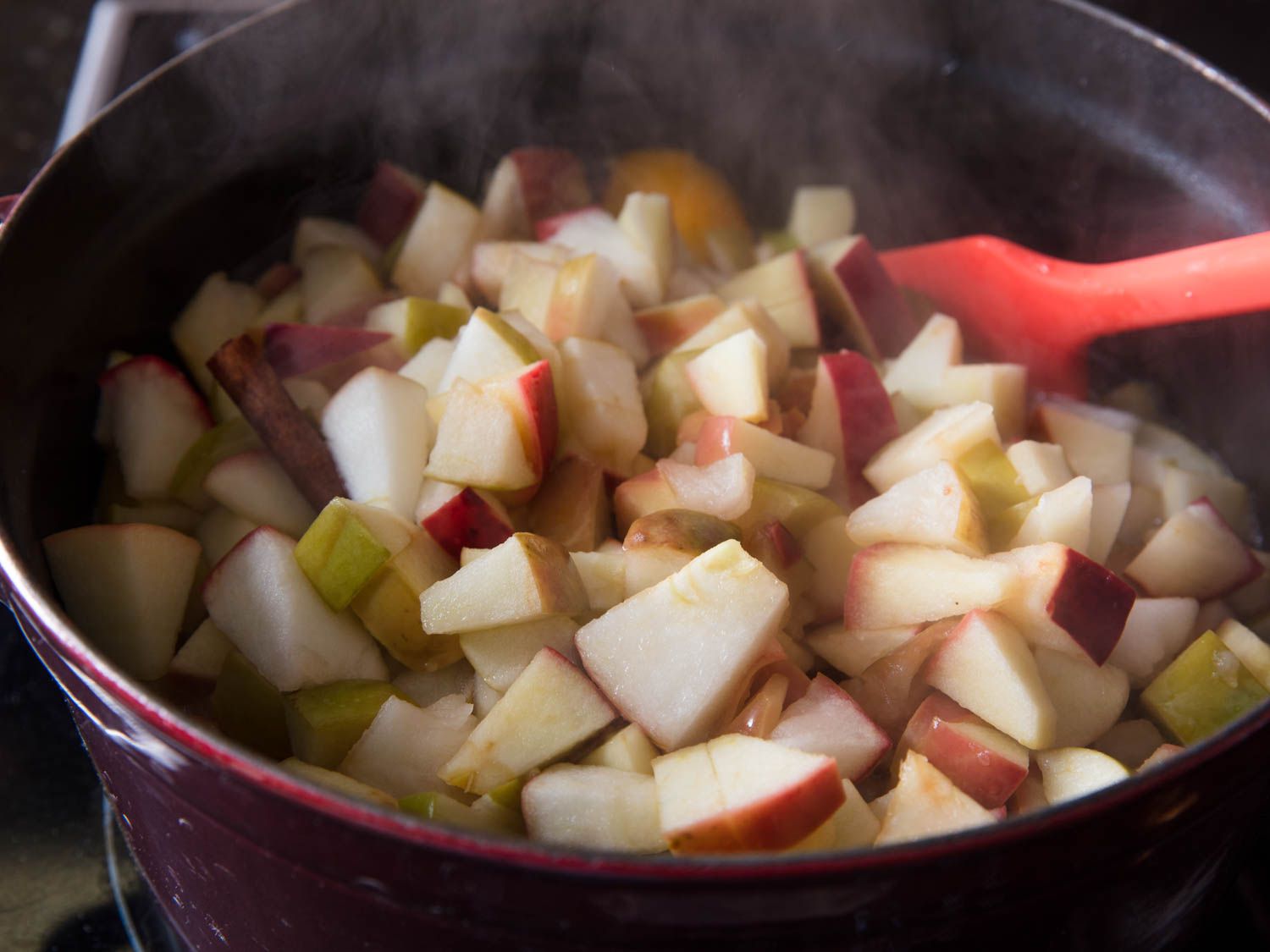 一锅用来做苹果酱的大块苹果，锅子里插着一把红色的锅铲