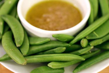 A bowl of anchoïade surrounded by sugar snap peas.