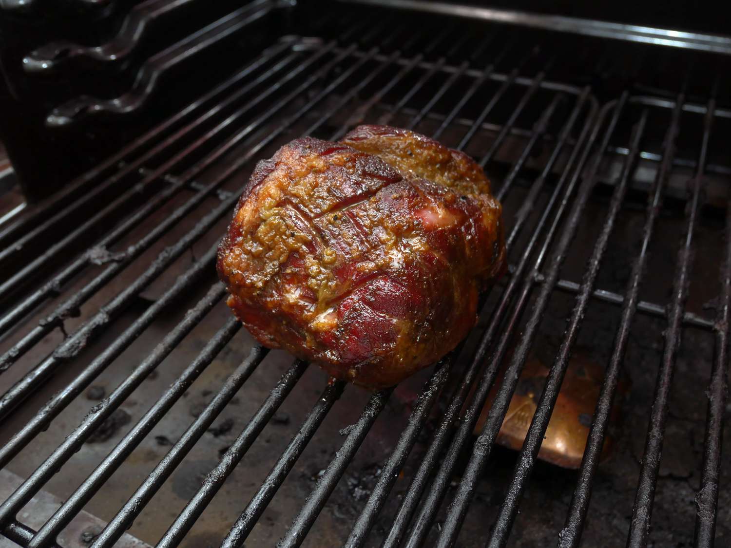 a closeup of a small smoked pork shoulder on the smoker grill grates