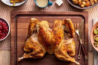 Spatchcocked Turkey on a wooden carving board surrounded by Thanksgiving dishes