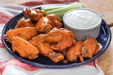 Sous vide Buffalo chicken wings on a blue plate with cup of blue cheese dressing and celery sticks on the side.