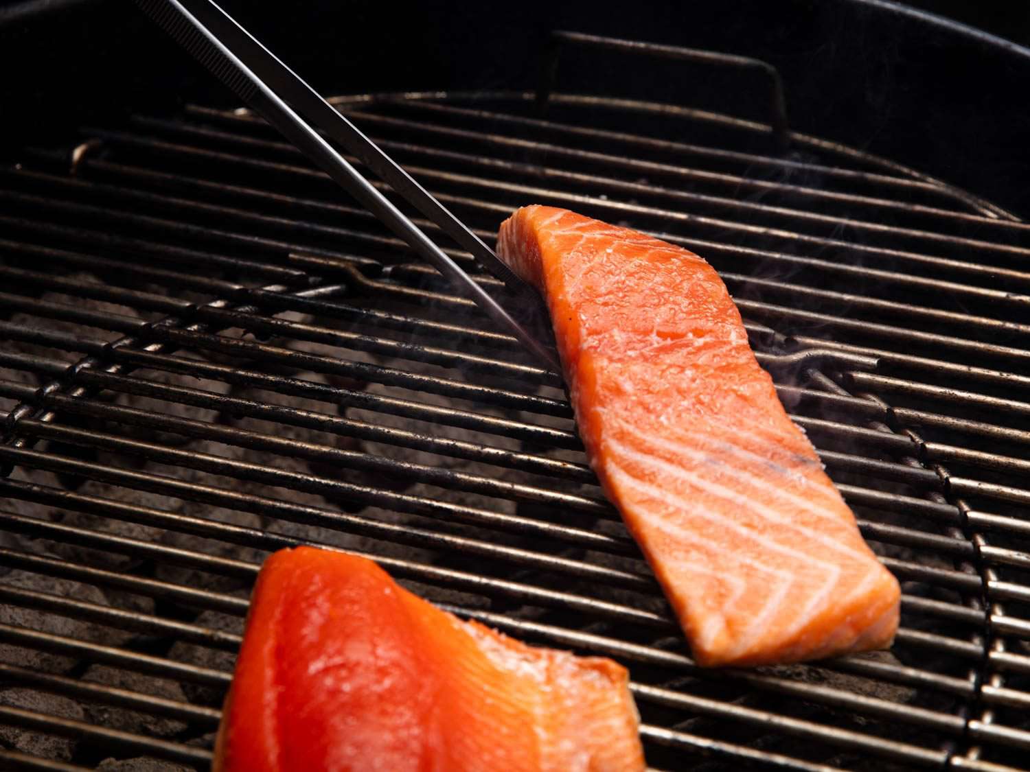 用烹饪用的镊子从下面夹起一片三文鱼，把它放到烤架上。