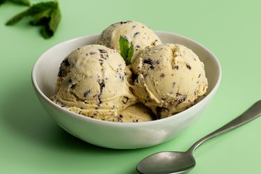A white porcelain bowl holding three scoops of mint chocolate chip ice cream.