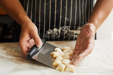 Using the OXO bench scraper to scrape up gnocchi dough on a floured marble countertop