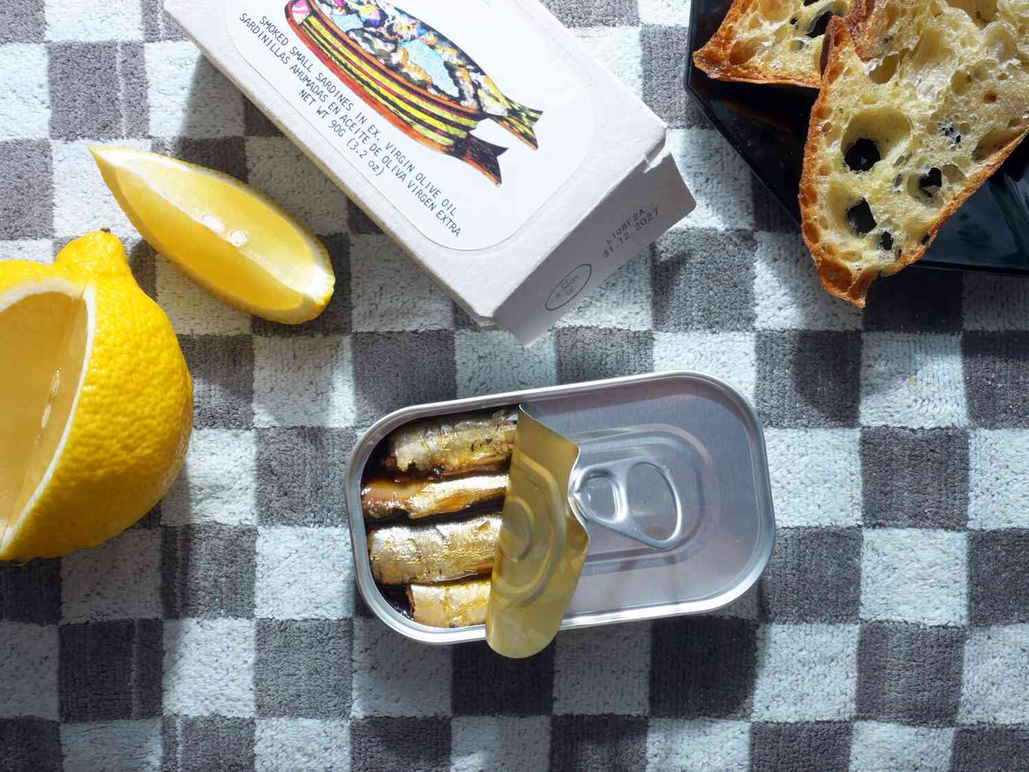 an open tin of fish with a lemon wedge and slices of bread