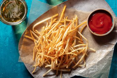 在head view of shoestring fries on wax paper on a platter with a ramekin of ketchup and a glass of beer alongside