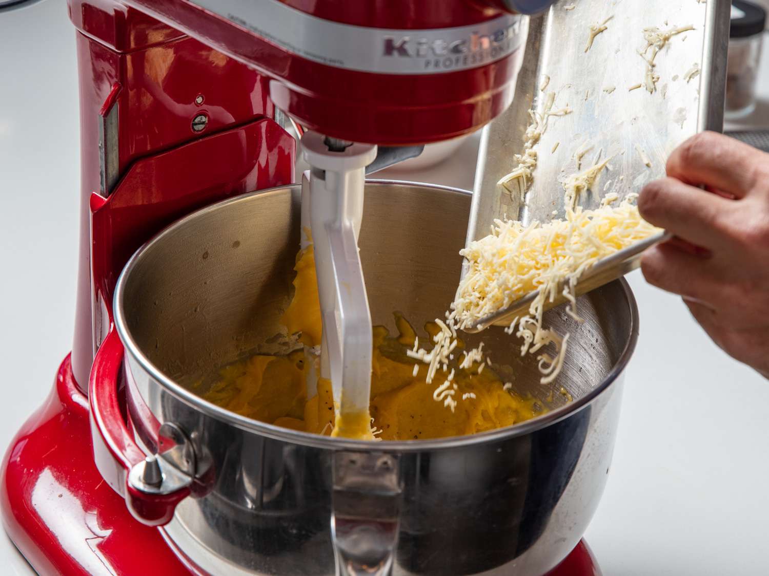Shredded cheese is added to the stand mixer bowl.