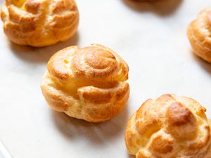 Freshly baked choux pastry puffs on a parchment lined baking sheet.