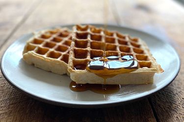 Two sourdough waffles on a plate with maple syrup