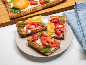 Slices of tomato tart on a plate, set in front of a cutting board with the rest of the tomato tart