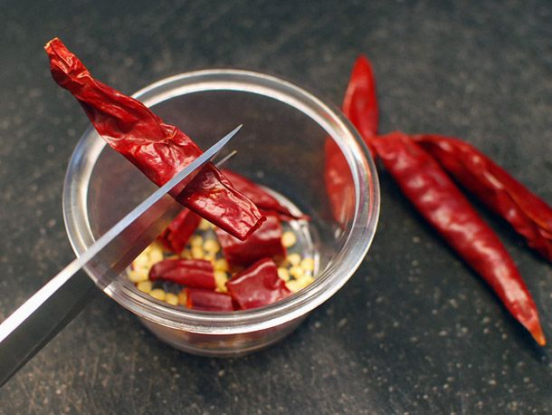 一把厨房剪刀正在切干辣椒，俯瞰着盛着辣椒籽和辣椒段的碗。