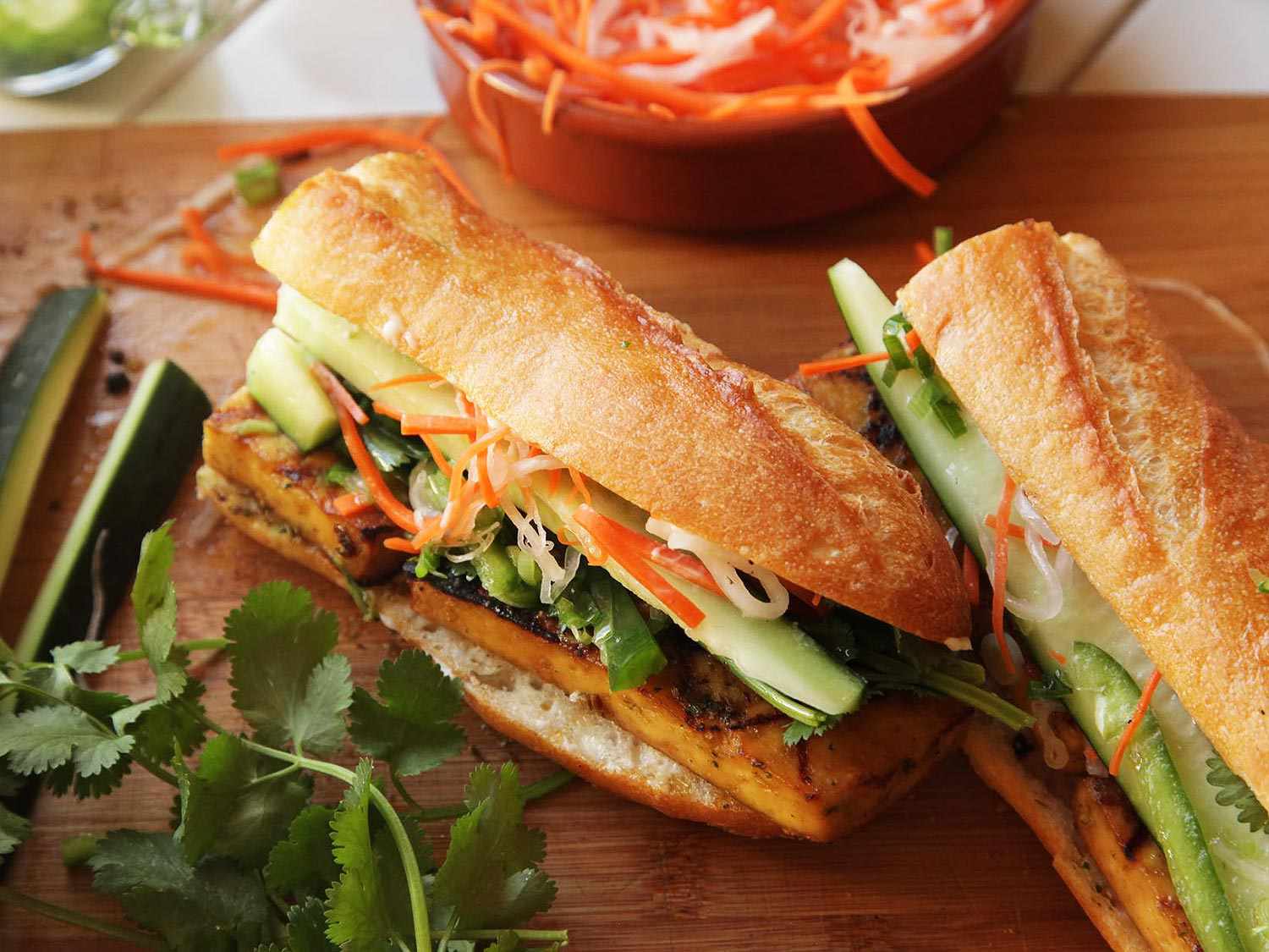 烤豆腐越南三明治的特写，里面有胡萝卜-白萝卜泡菜和黄瓜矛。香菜就在手边。
