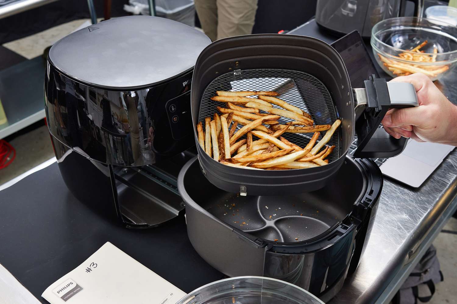 a hand holding an air fryer basket full of fries