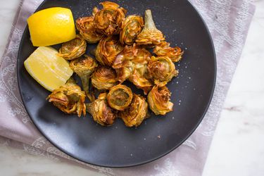 Overhead view of fried artichoke hearts plattered with lemon wedges