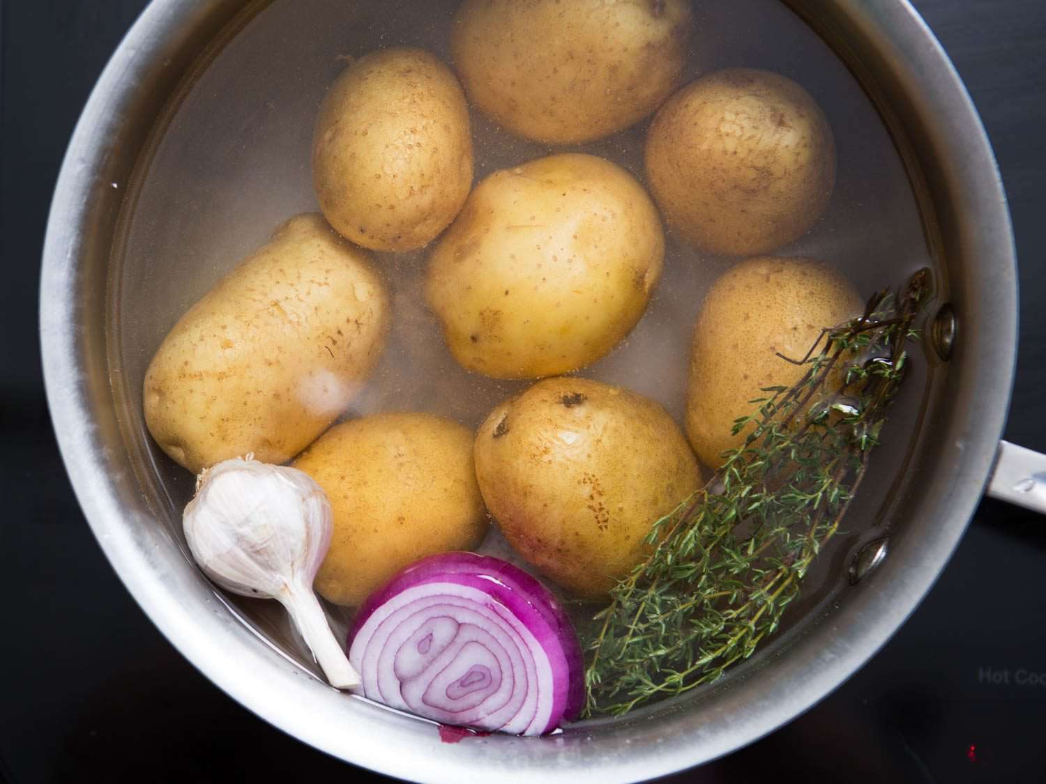 Potatoes in pot of water with garlic, shallot, and rosemary.