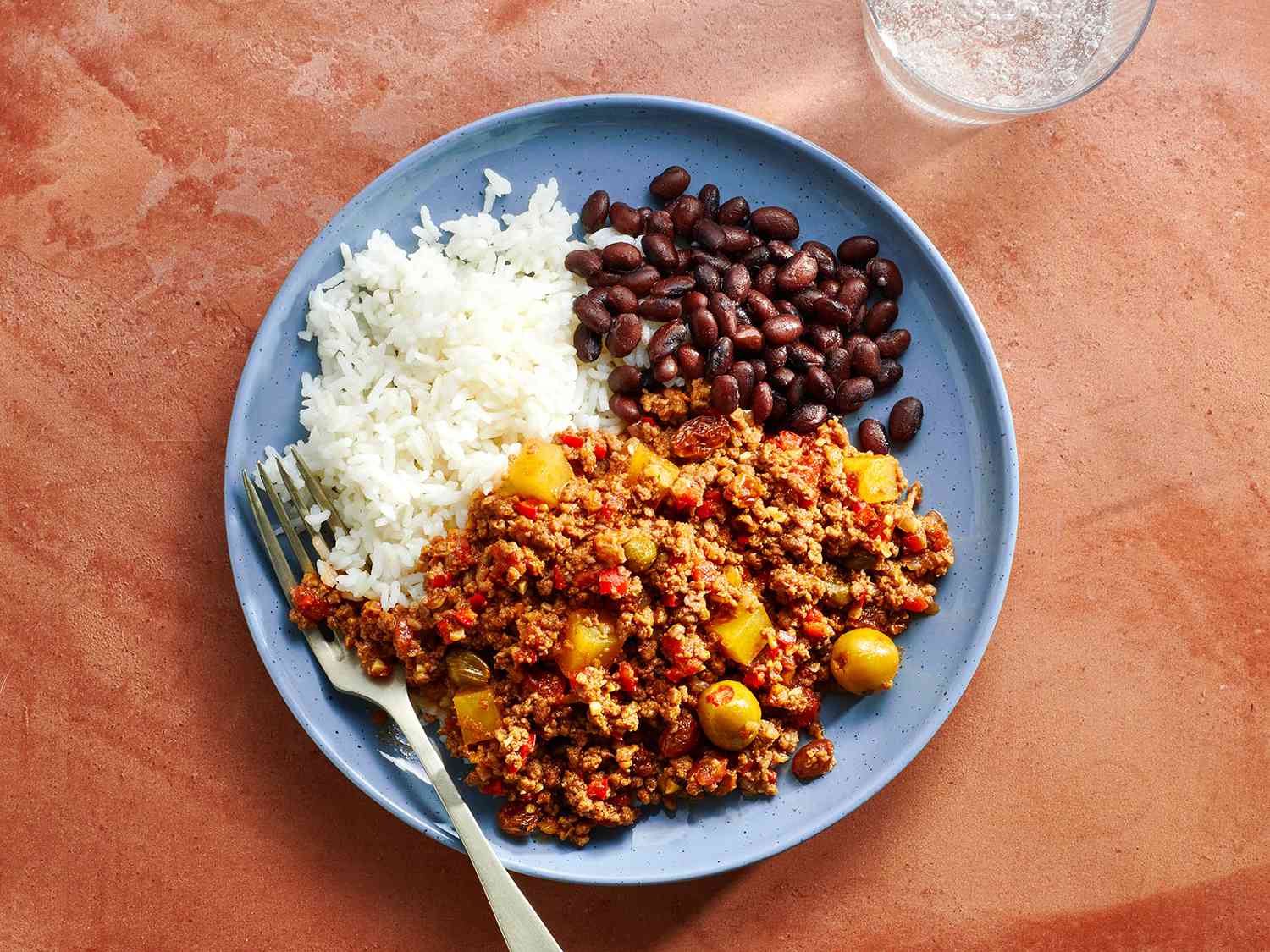 A blue ceramic plate with picadillo, white rice, and black beans.