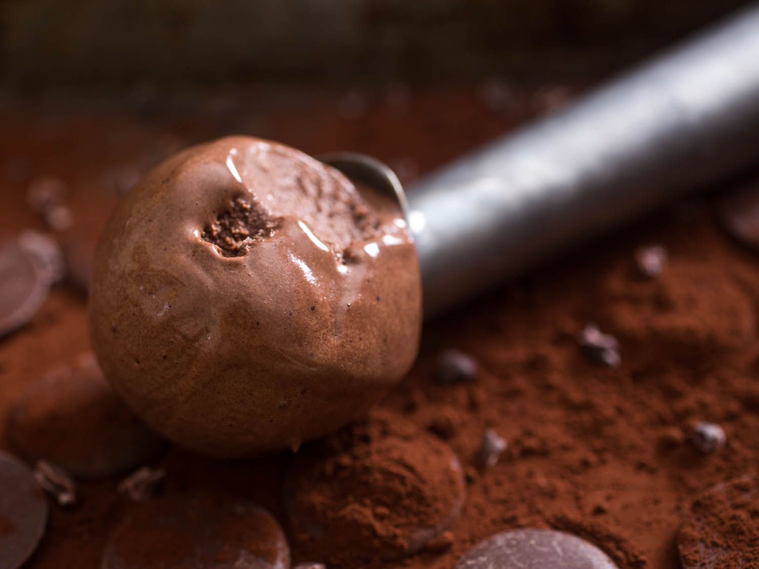 一勺最黑的黑巧克力冰淇淋，背景是可可粉、巧克力片和巧克力盘。
