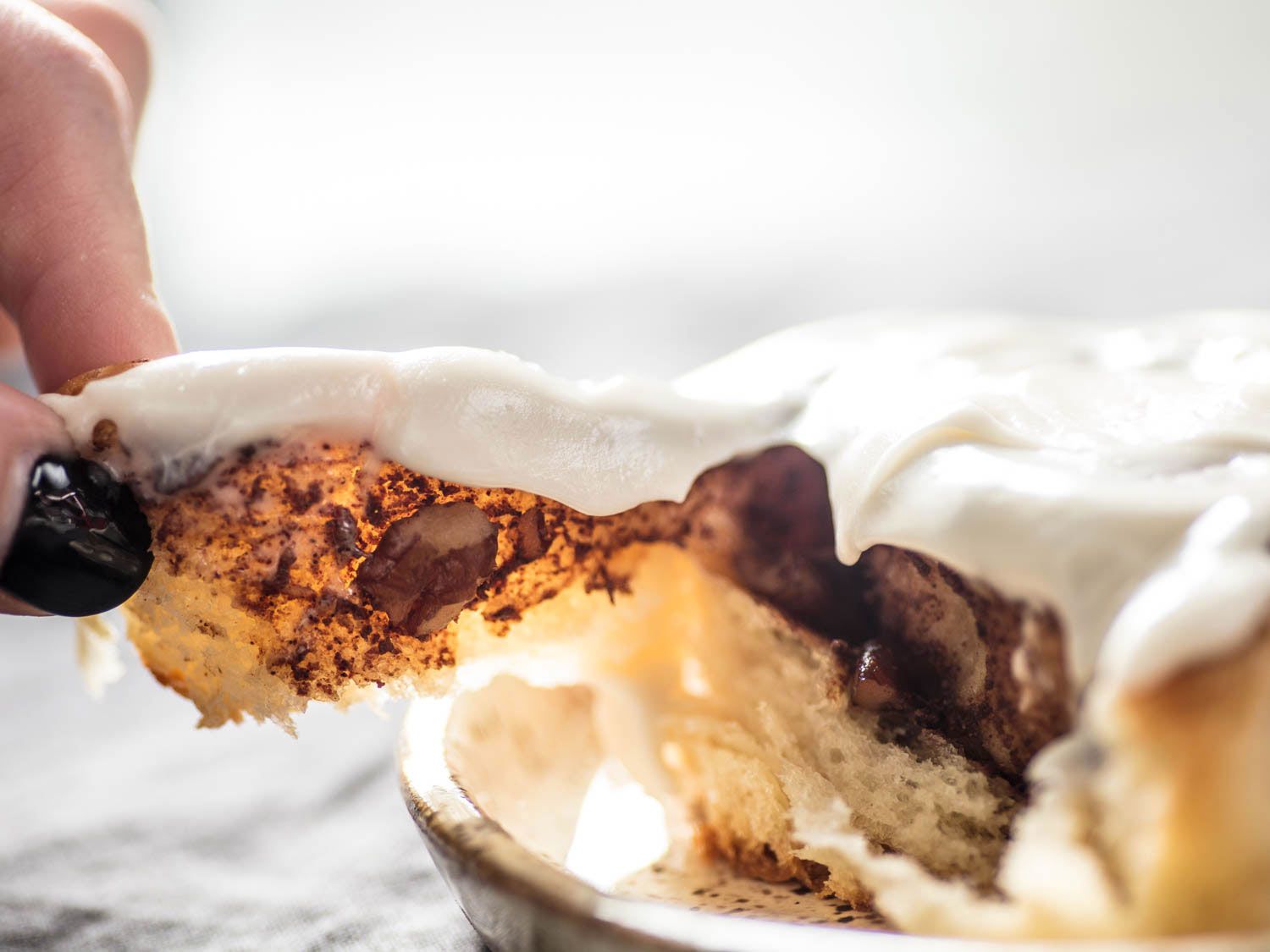 A hand pulling off a portion of freshly baked cinnamon roll.