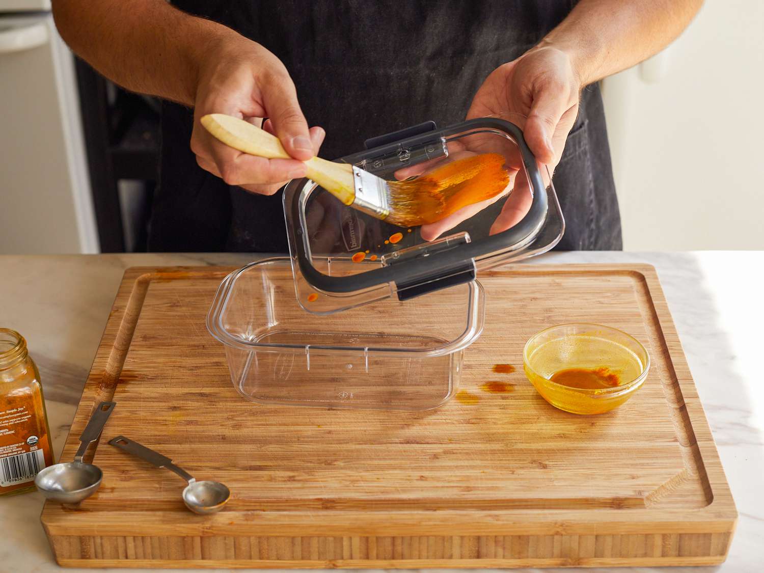 一只手正在用糕点刷将油和姜黄的混合物涂在食品储存容器的盖子上