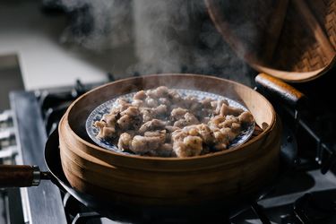 A bamboo steamer set in a wok holds a plate of freshly steamed pork ribs.